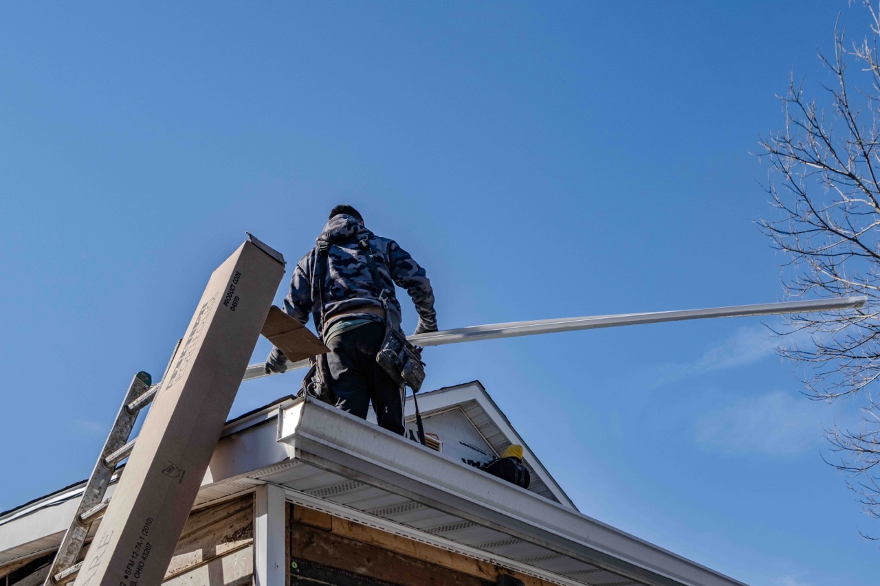 siding technician holding a piece of siding while on a one story home