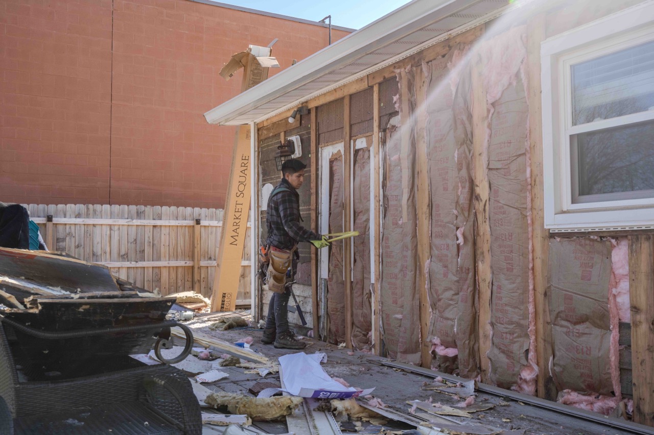 siding technician using a tape measure to measure in between the studs of an exposed home exterior.