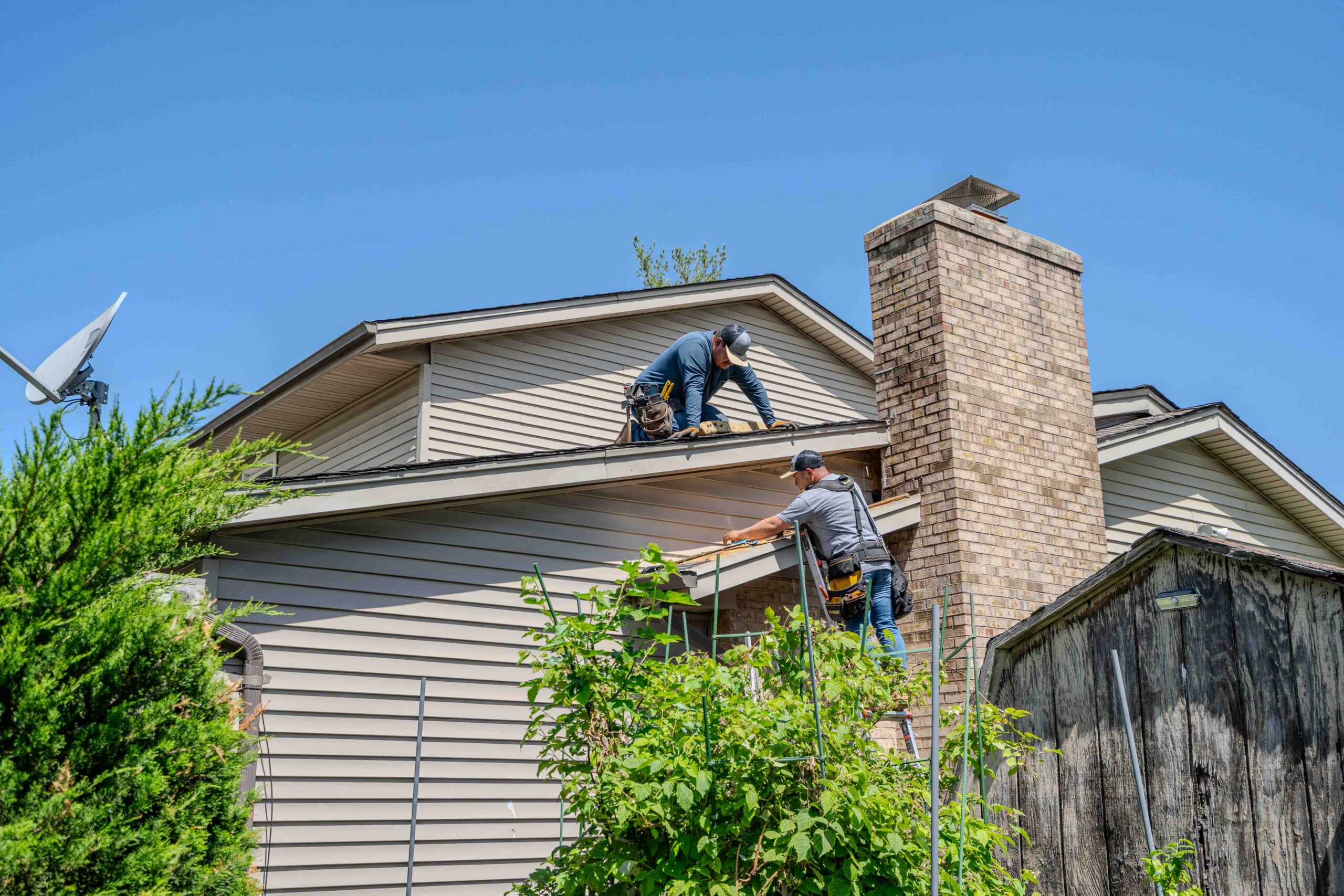 two roof technicians on a two story building repairing chimney flashing